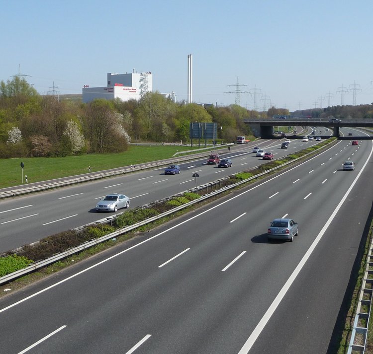 Autobahnen führen unter einer Brücke hindurch. Im Hintergrund ist ein Industriestandort