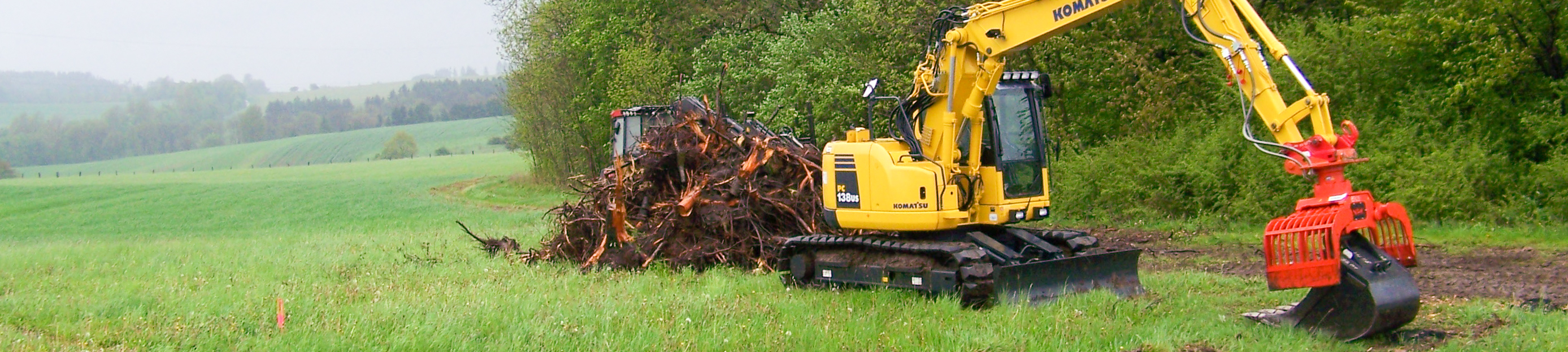 Ein Bagger steht auf einer Wiese neben Pflanzensschnitt